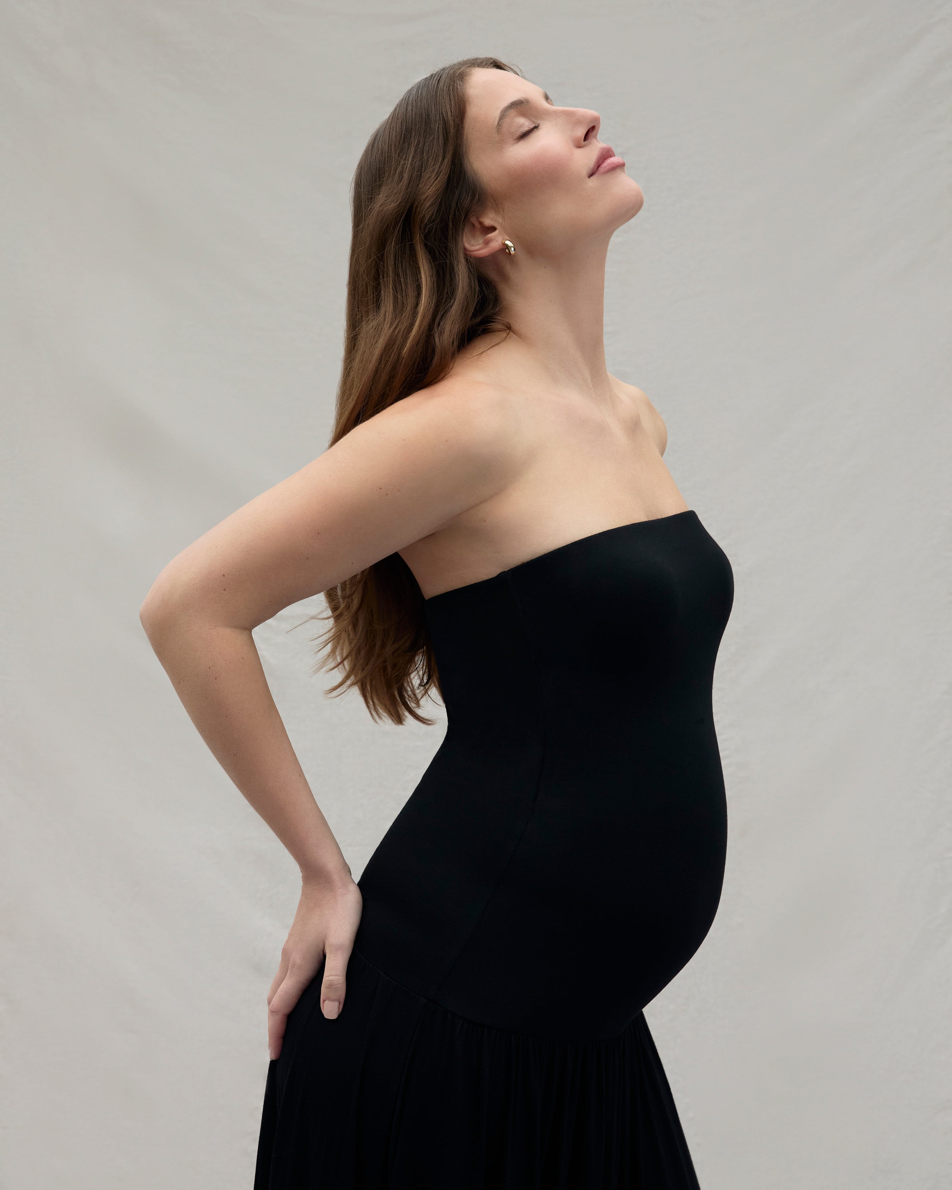 Woman wearing a black strapless dress against a plain background