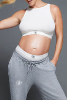 Person wearing a white sports bra and gray sweatpants with a Bumpsuit logo on a gray background