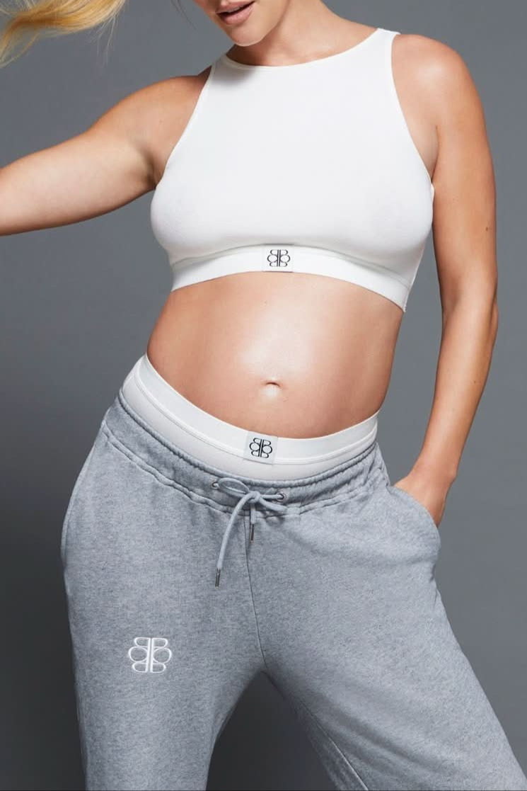 Person wearing a white sports bra and gray sweatpants with a Bumpsuit logo on a gray background