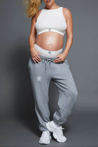 Pregnant person wearing a white Bumpsuit crop bra and grey sweatpants on a grey background