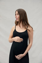 pregnant woman wearing a Bumpsuit black jumpsuit holding her belly and looking away