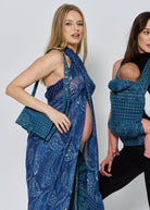 Two women wearing the spell and bumpsuit collaboration, one with a baby carrier and another with a. dress scarf and bag in a blue print