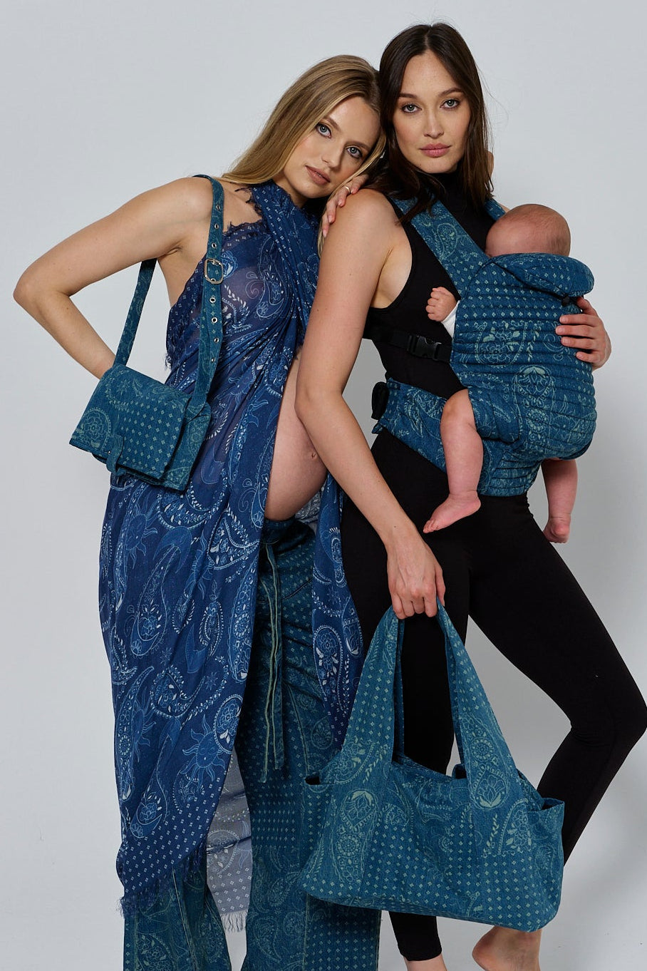 Front view of Mom-On-The-Go Bag in blue denim print with shoulder strap, worn by a model beside a baby carrier