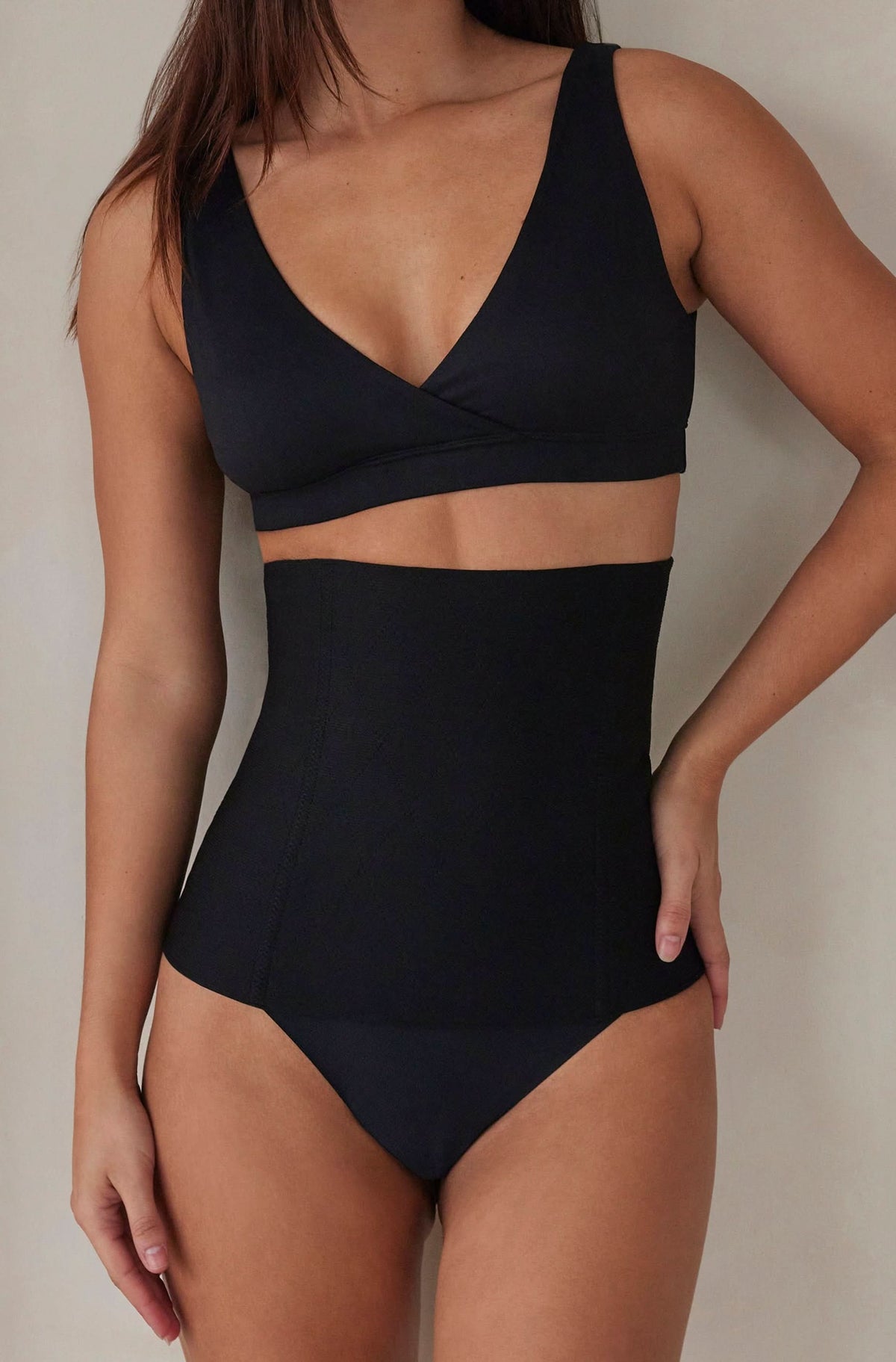 Woman wearing the postpartum support waist trainer in black by bumpsuit