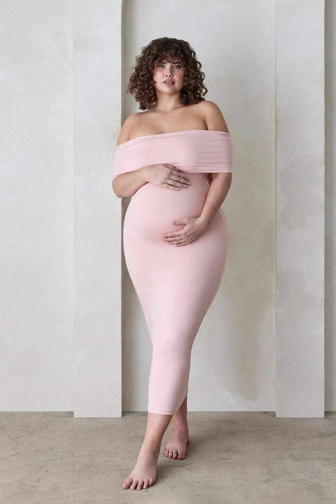 Pregnant woman wearing the Bumpsuit Maternity The Bianca Off Shoulder Maxi Dress in Dusty Pink