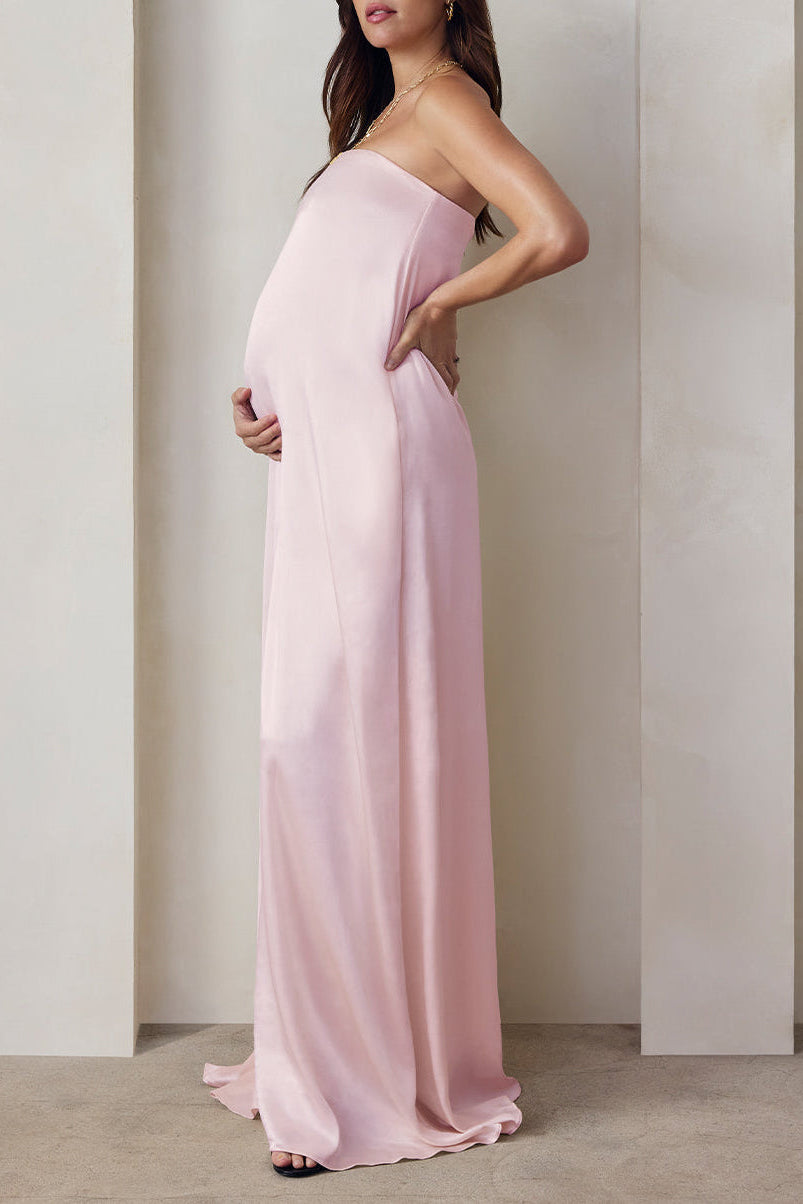 A pregnant woman wearing the Bumpsuit brushed satin strapless maxi maternity gown in dusty pink against a beige feature wall