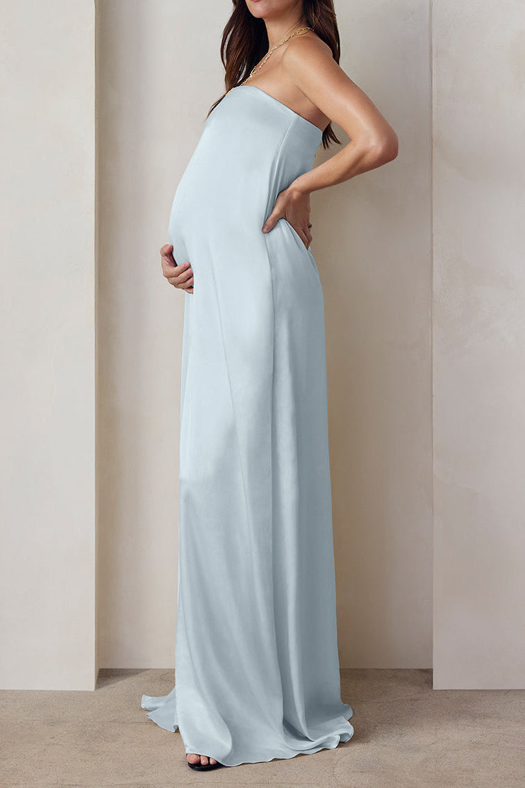 A pregnant woman wearing the Bumpsuit brushed satin strapless maxi maternity gown in powder blue against a beige feature wall