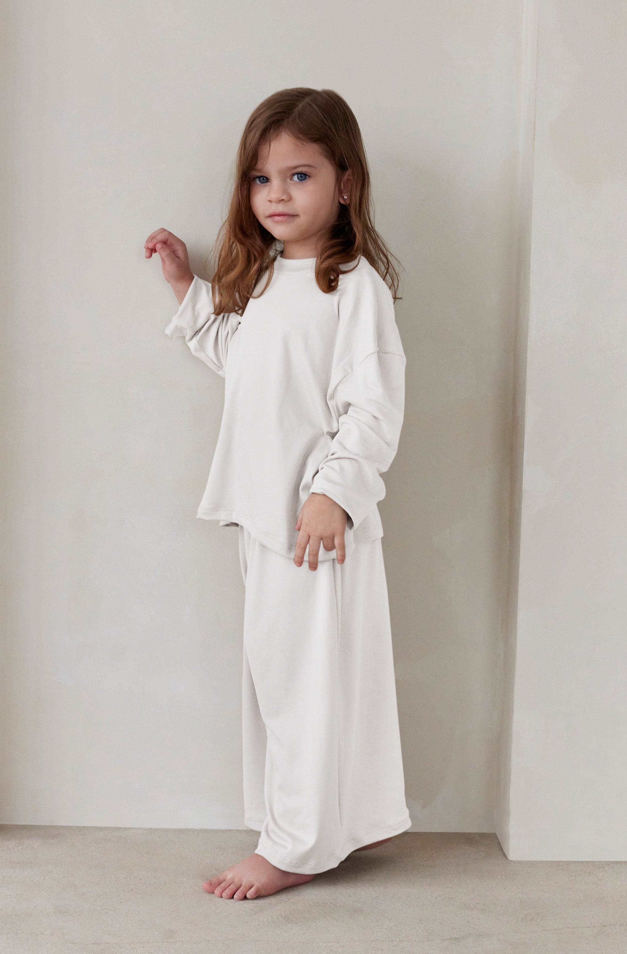 Young child wearing a white outfit standing against a plain background