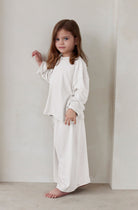 Young child wearing a white outfit standing against a plain background