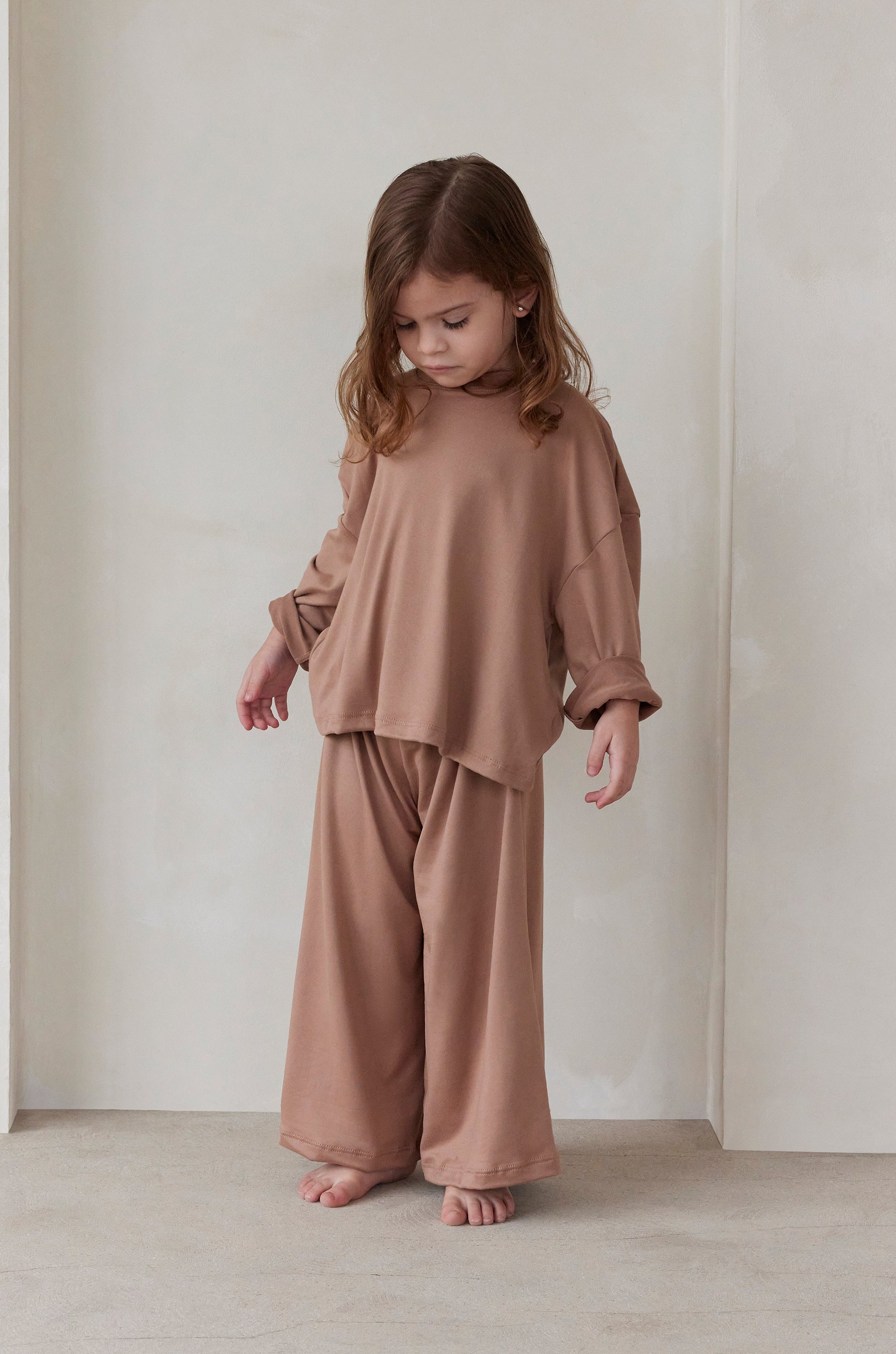 Child wearing a latte brown bumpsuit pyjamas standing against a plain background