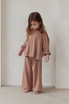Child wearing a latte brown bumpsuit pyjamas standing against a plain background