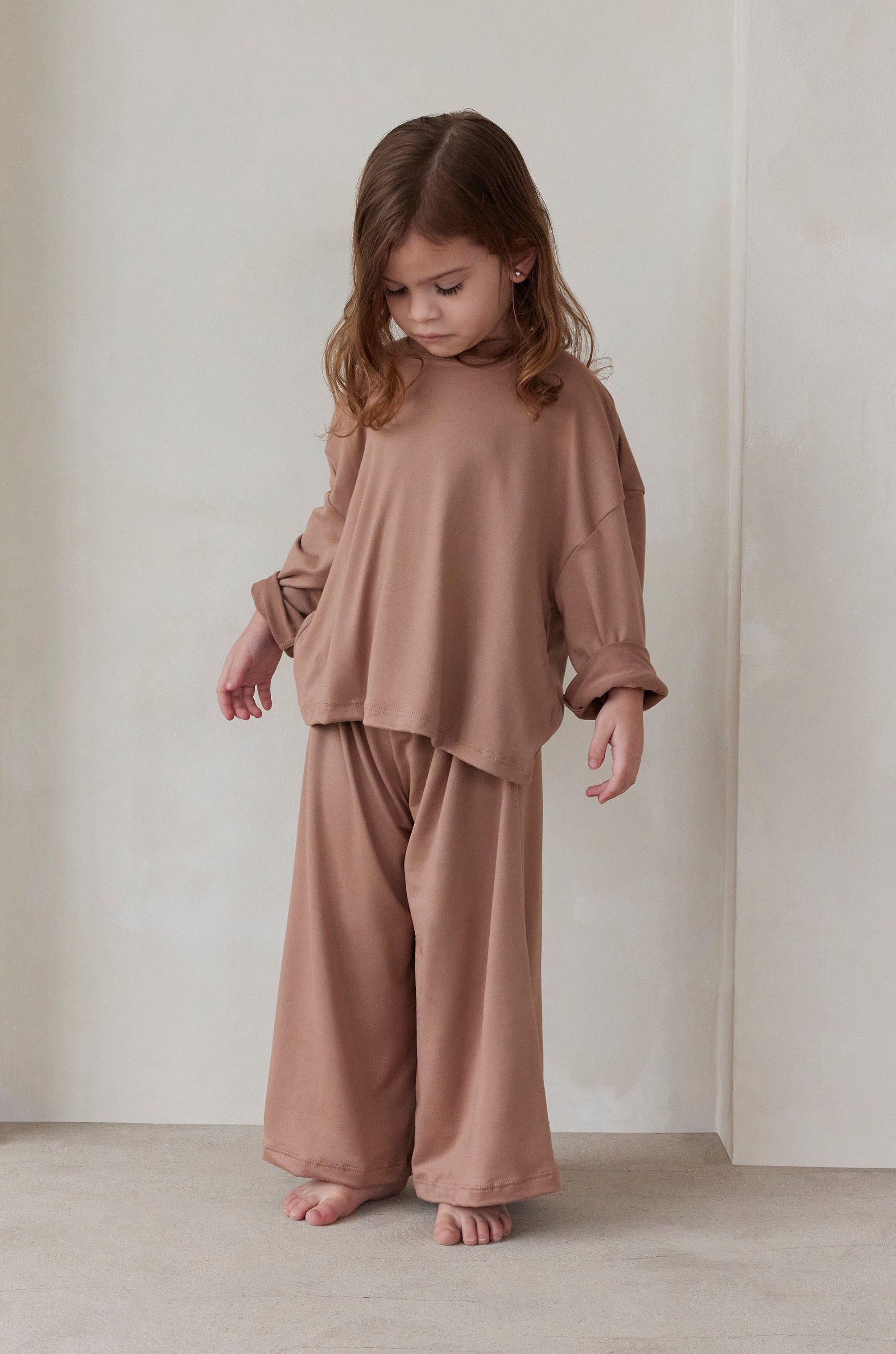 Child wearing a latte brown outfit standing against a plain white wall