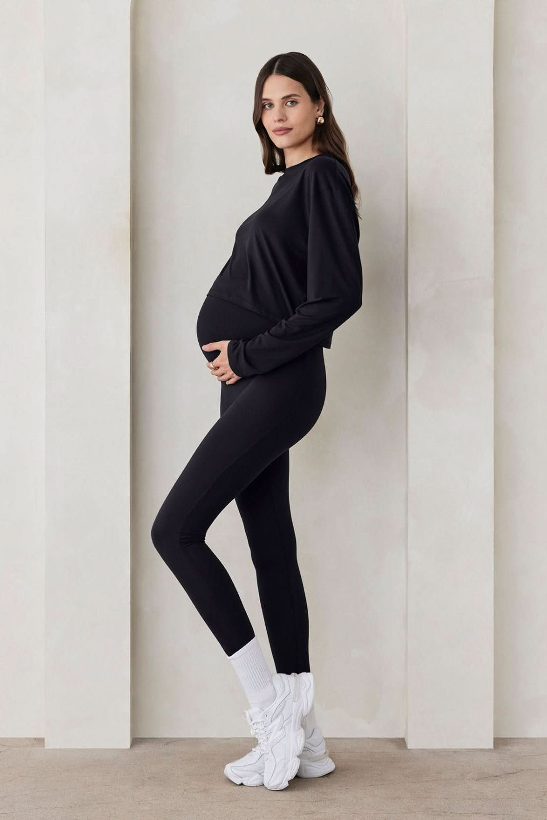 Side view of Bumpsuit The Maternity Legging in black showcasing full-body length on a pregnant model in a light studio
