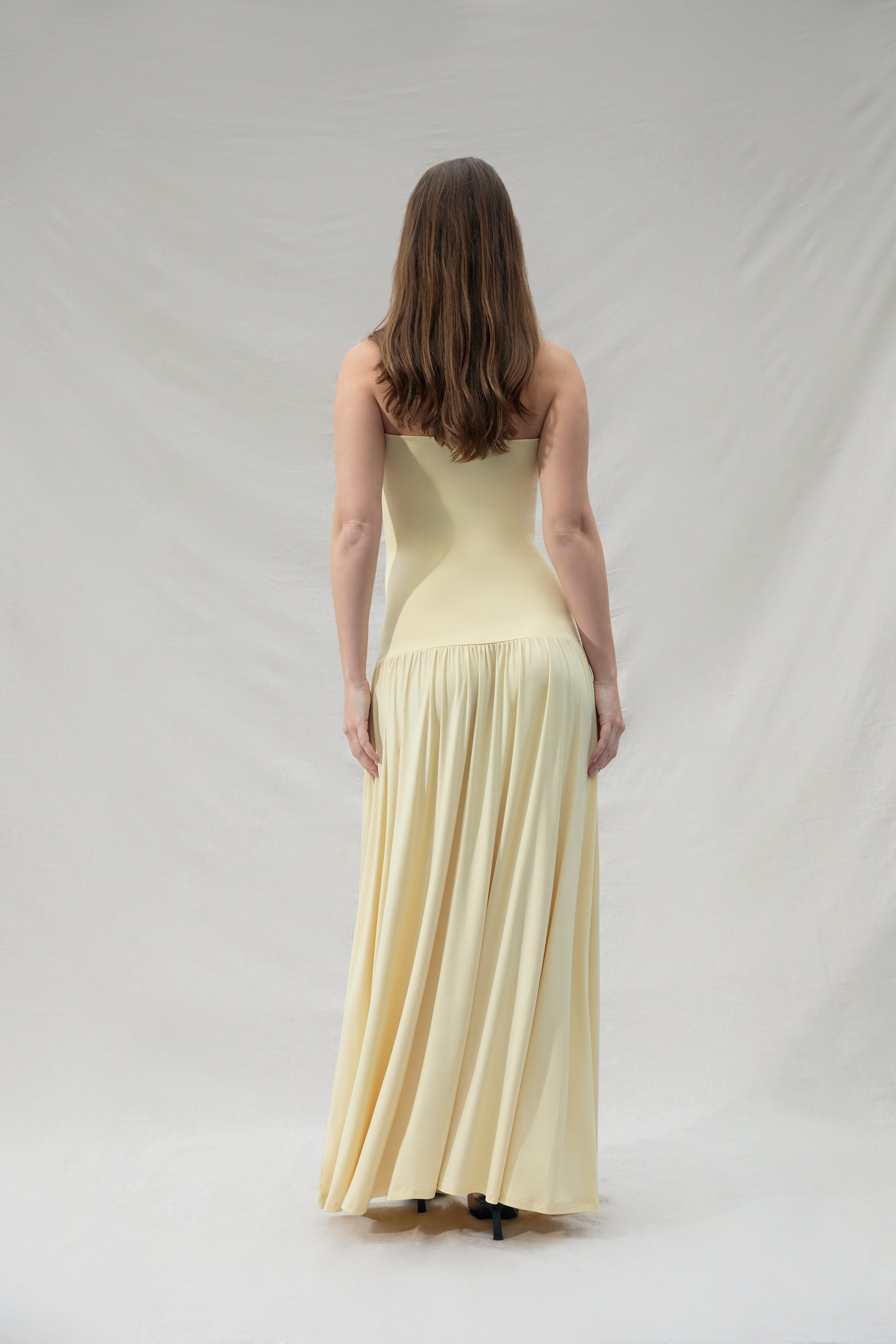 Pregnant woman wearing a maternity Bumpsuit strapless yellow dress against a plain background