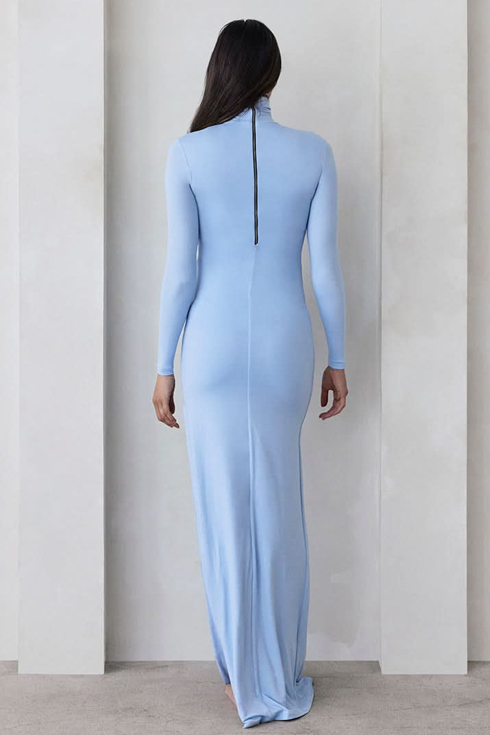 Back view of The Monica maternity dress in powder blue, showing center-back zipper and floor-length fit against a gray wall