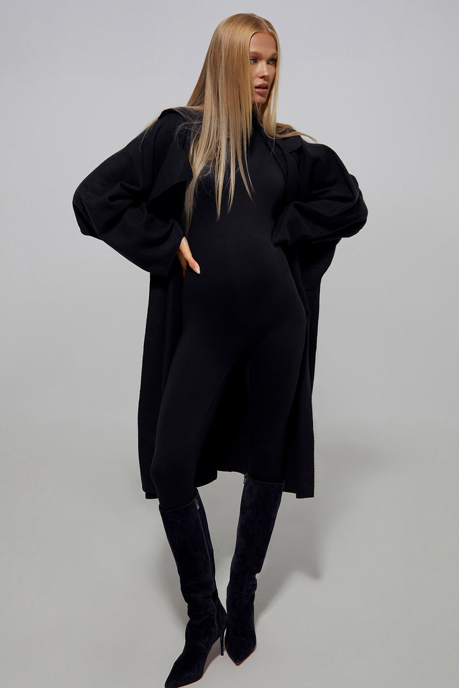 Model Vita Sidorkina wears the Bumpsuit penelope maternity turtleneck longsleeve jumpsuit in black with a long coat