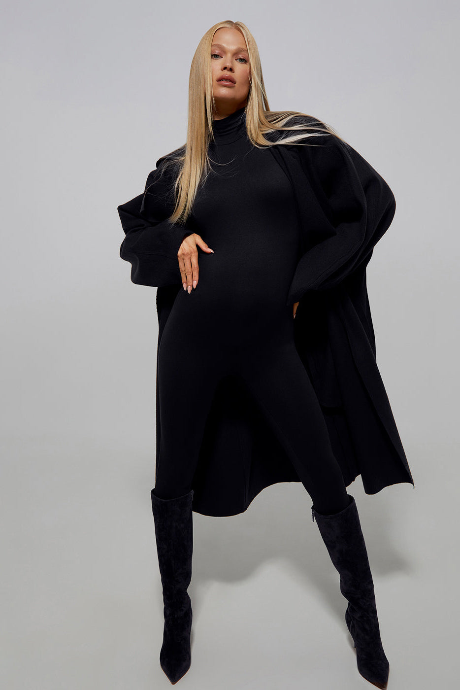 Model Vita Sidorkina wears the Bumpsuit penelope maternity turtleneck longsleeve jumpsuit in black with a long coat